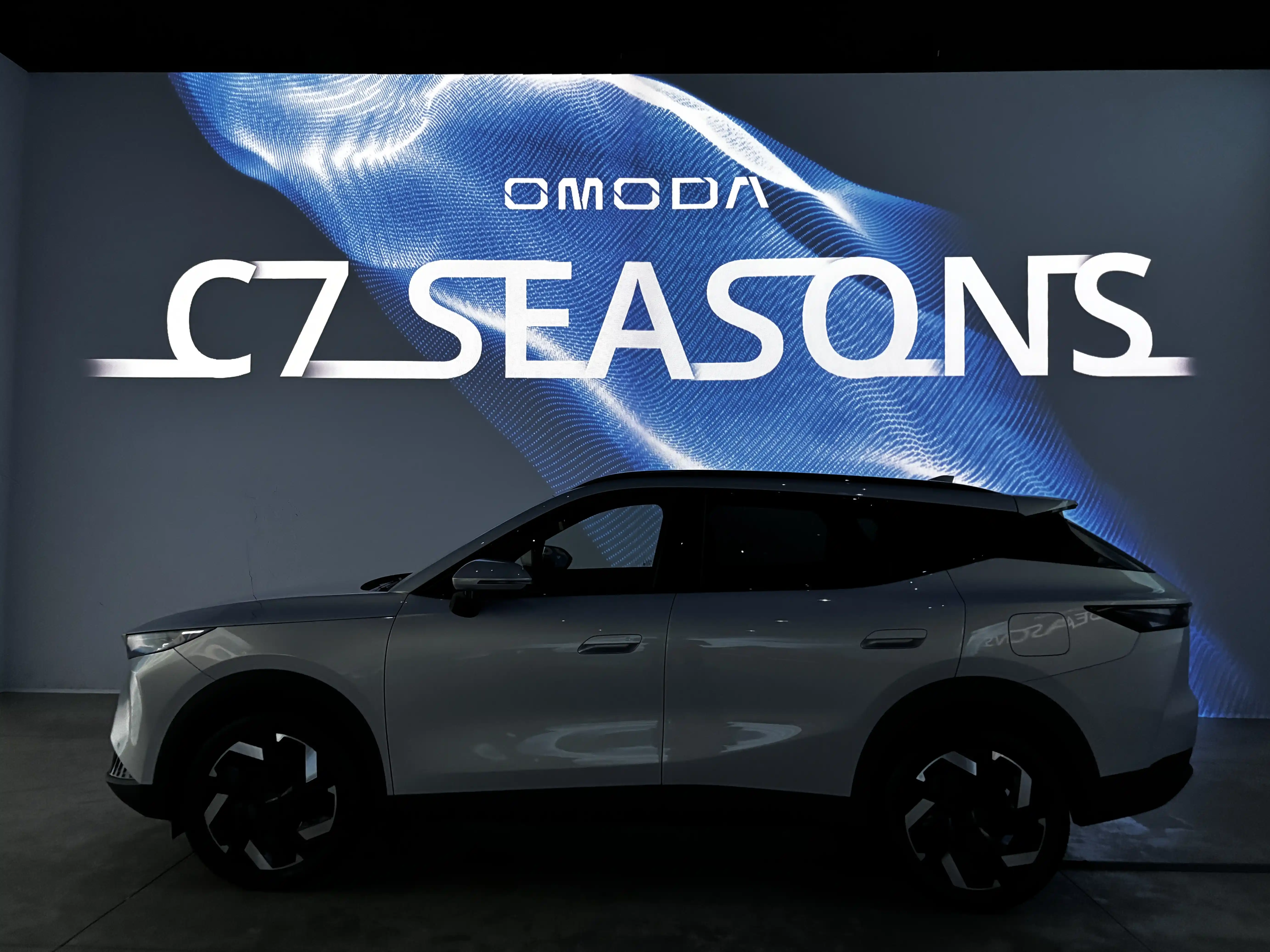 Автомобиль OMODA C7 на фоне экрана с графикой SEASONS