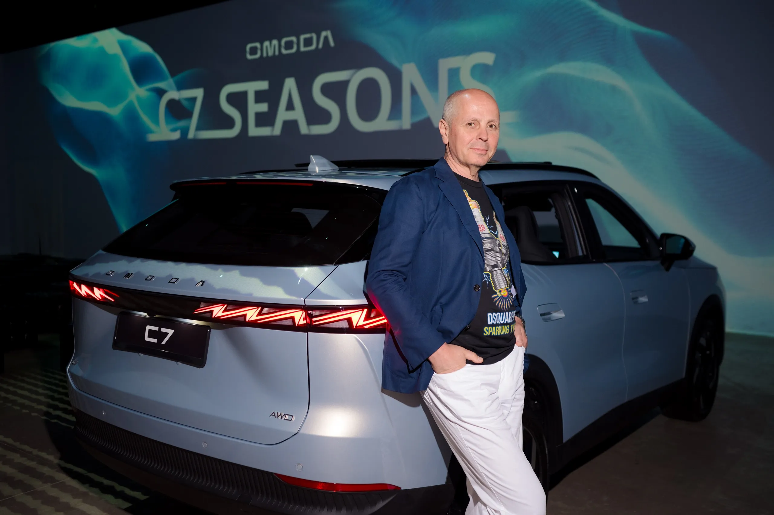 Гость позирует рядом с автомобилем OMODA C7 на презентации